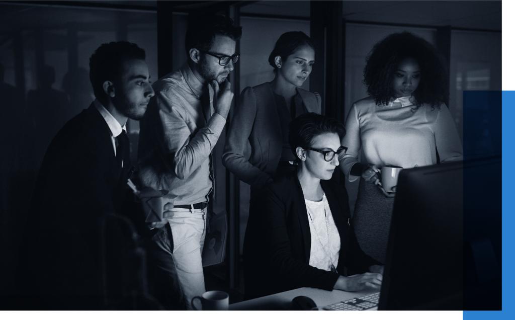 Concerned team of five mostly standing observing the screen of one seated teammate working on a computer at night